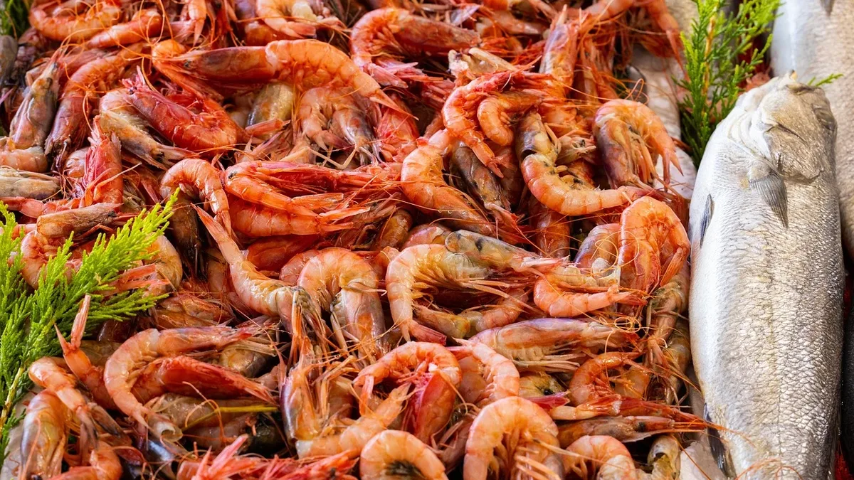 A large pile of shrimp and two fish, with some greenery visible on the left and right sides.